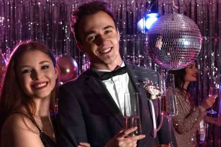 high school prom couple smiling for the camera with a disco ball behind them.